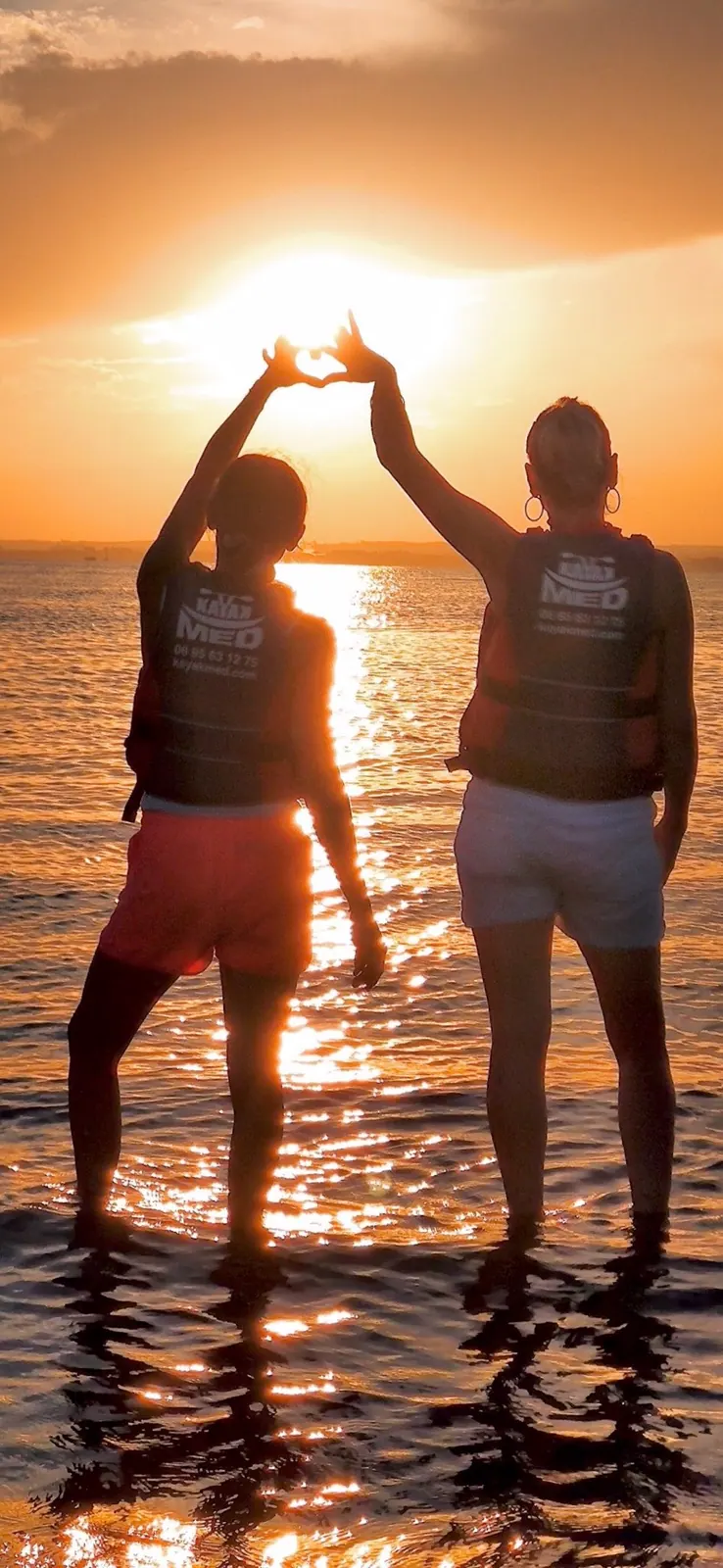 Couple en paddle, mains levées devant le coucher du soleil